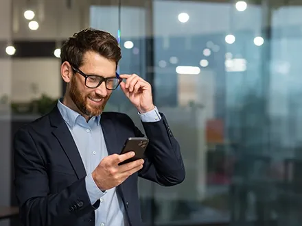 Mann checkt sein Handy im gläsernen Büro, fass mit Hand an die Brille.